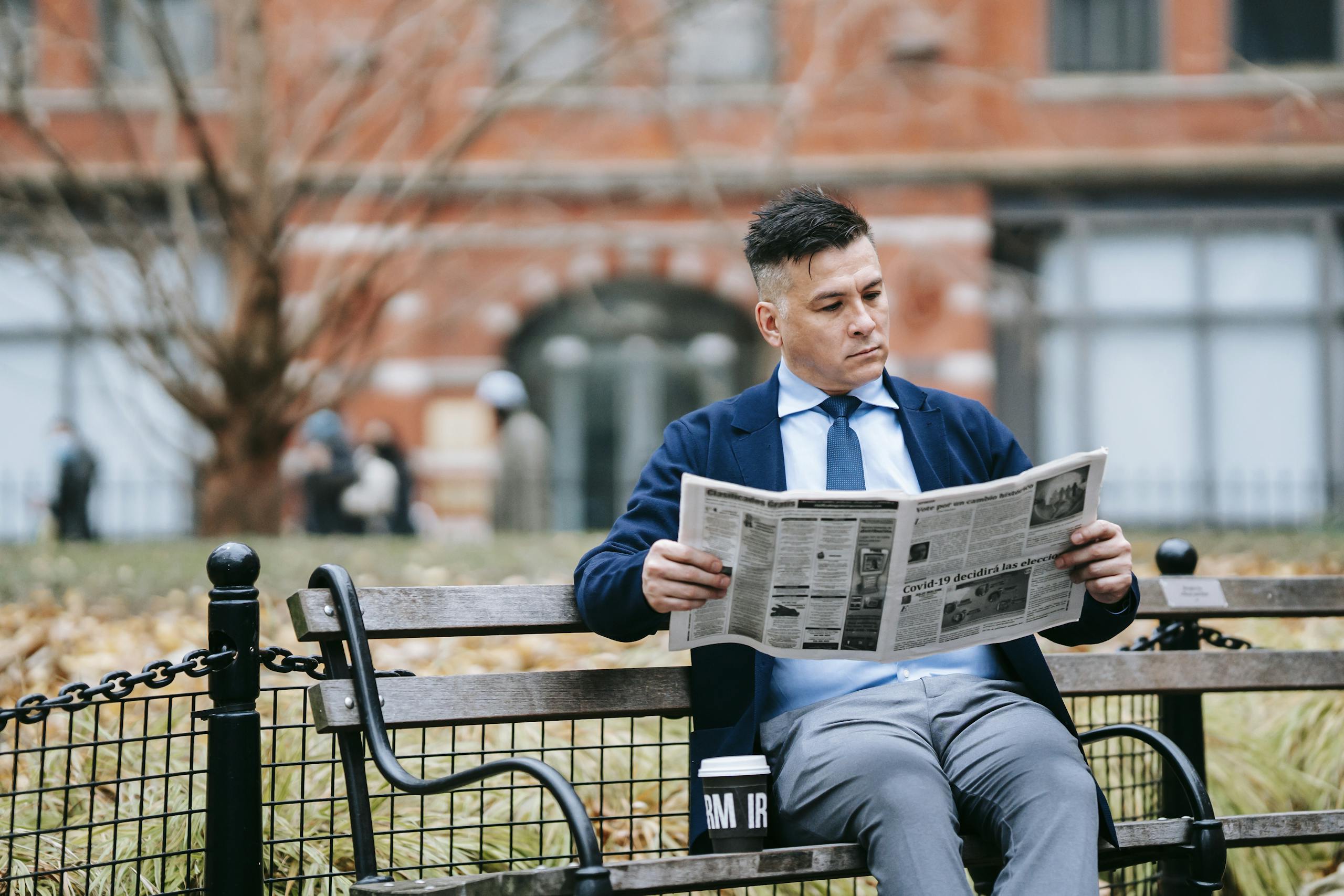 Corporate Governance News A man in formal attire sits on a park bench reading a newspaper, emphasizing leisure and professionalism.