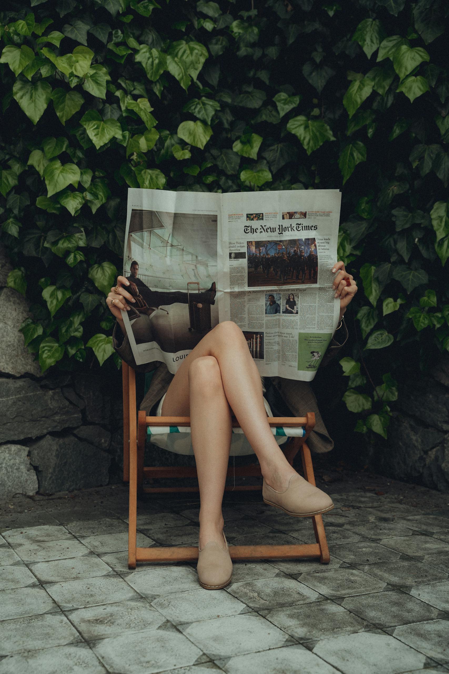 Transfer News A young woman relaxing in a garden chair reading a newspaper, symbolizing leisure and relaxation.
