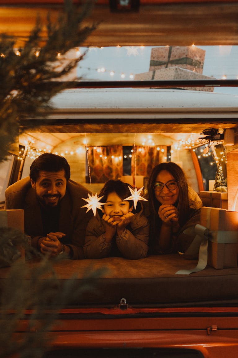 Family enjoying a festive holiday night in a decorated van with warm lights and gift boxes.