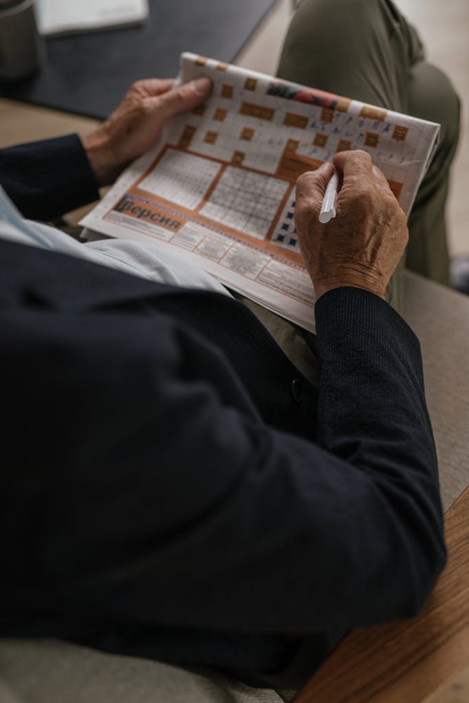 Universal Crossword  Senior adult solving a crossword puzzle in a newspaper, captured indoors.