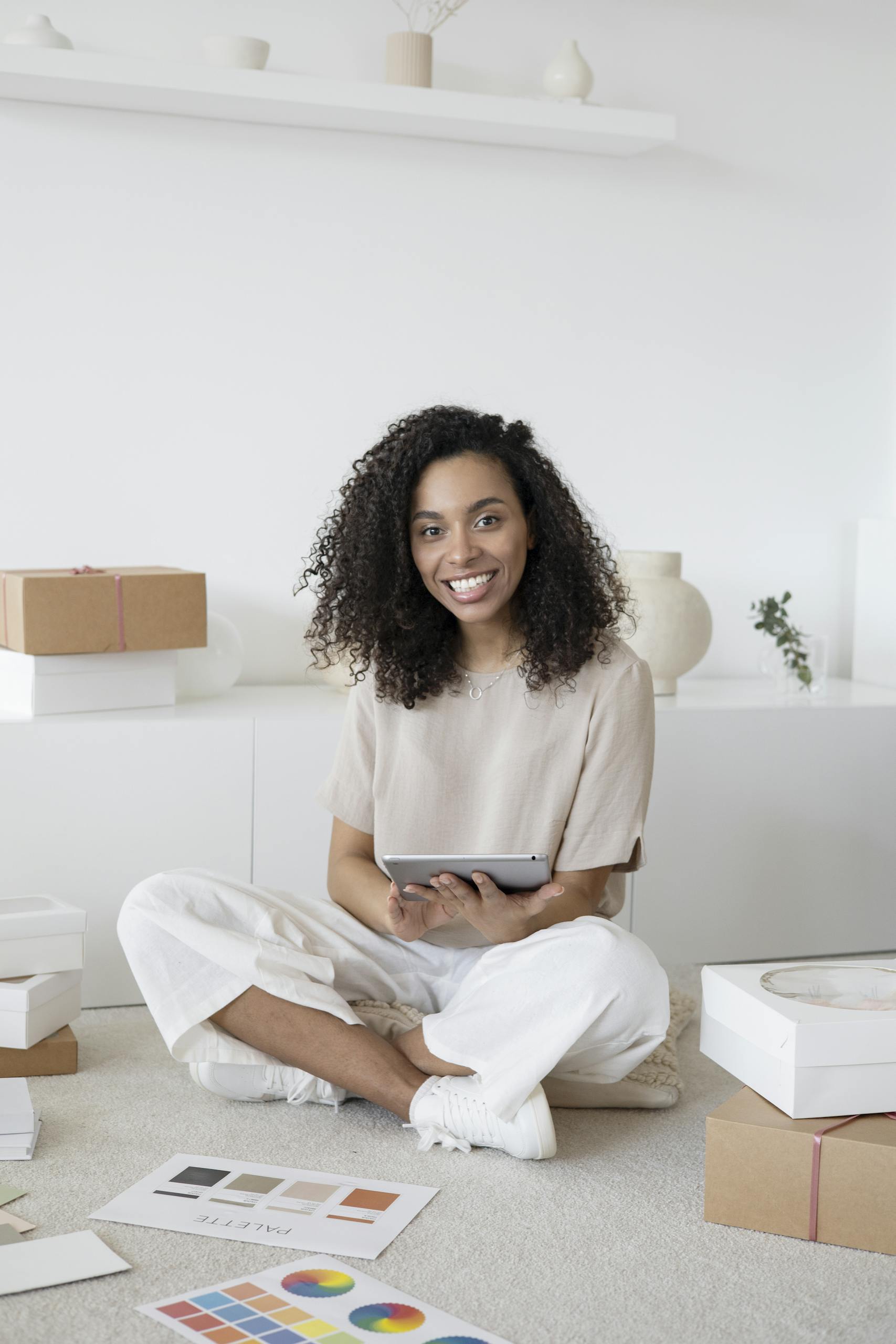 Twastia Com Owner A confident young woman sitting among packages and papers while using a tablet, showcasing modern entrepreneurship.