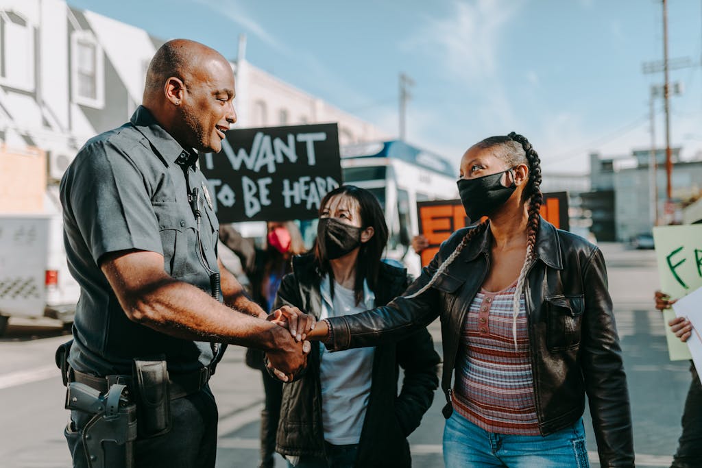 A police officer and a protester shake hands during a peaceful demonstration on a sunny day.