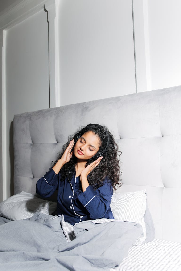 Pyjamaspapper A woman in pajamas enjoys listening to music while resting in bed, radiating comfort and relaxation.