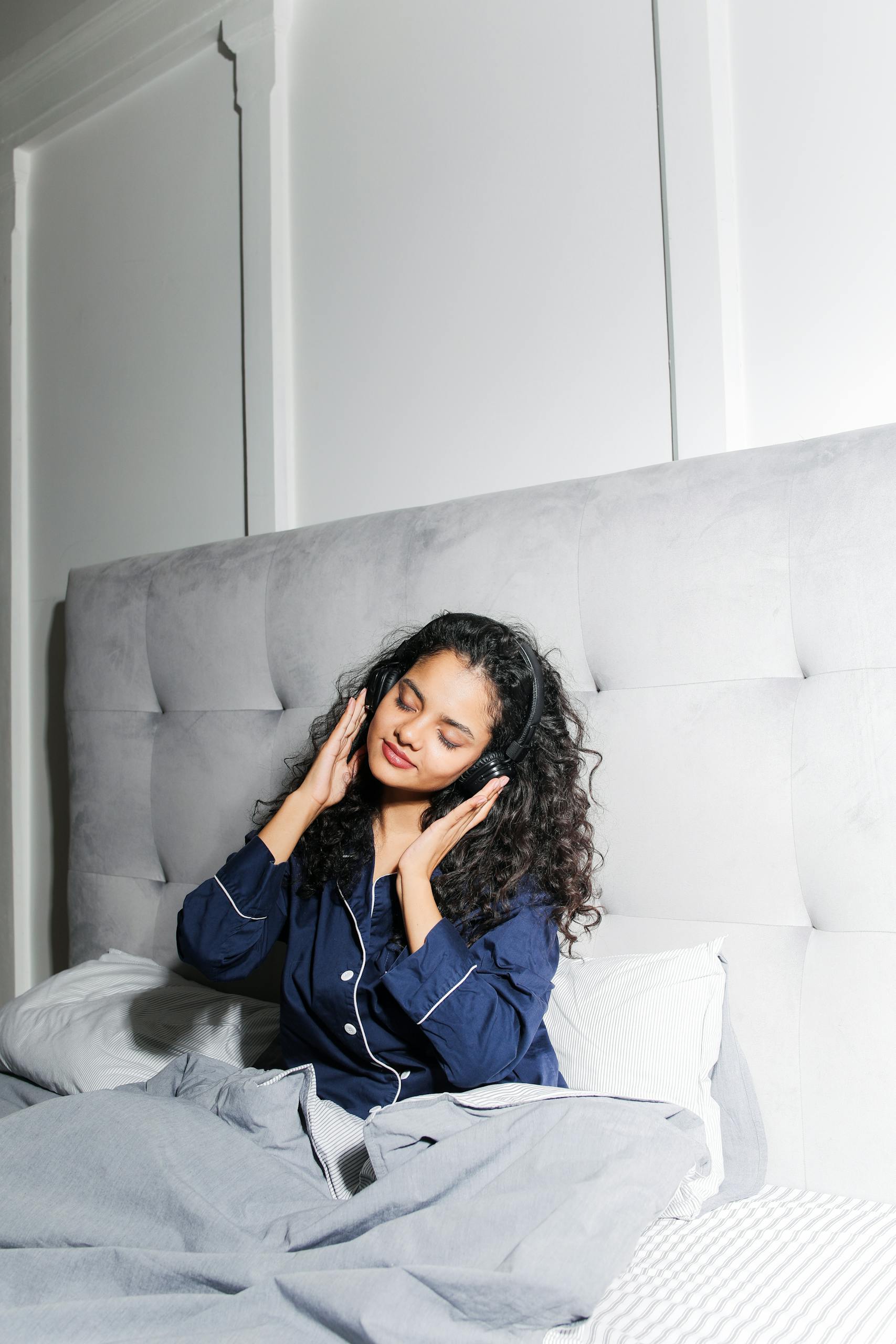 Pyjamaspapper A woman in pajamas enjoys listening to music while resting in bed, radiating comfort and relaxation.