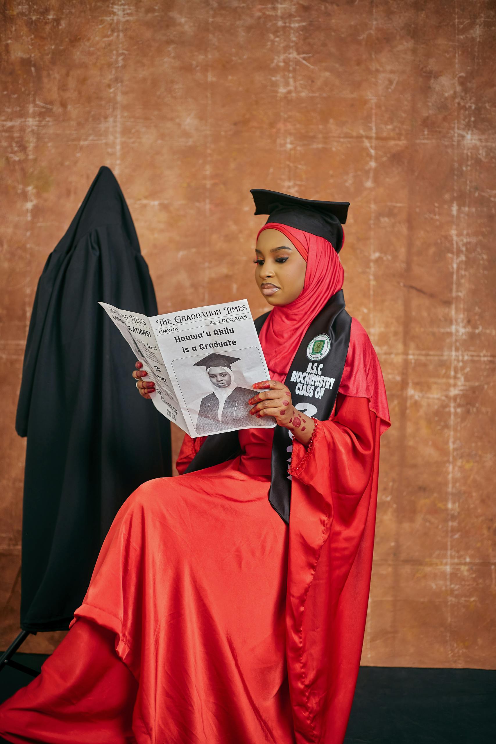 Rock band news A young woman in a red graduation gown reads a newspaper, celebrating her achievement.