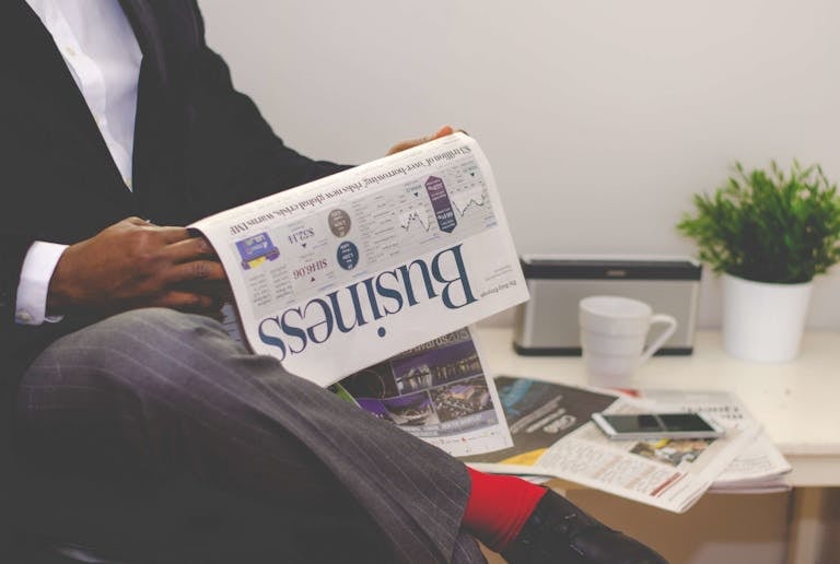 Newswell Businessman reading a financial newspaper at a desk, highlighting finance and commerce theme.