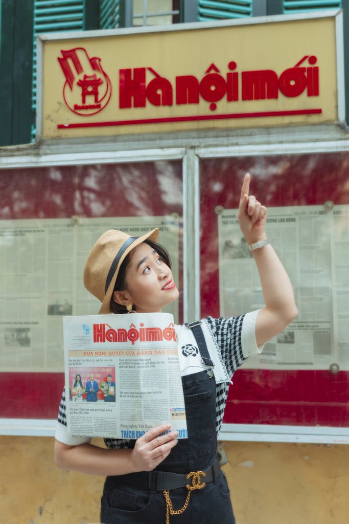 Casual woman holding and pointing at a Hanộimới newspaper in urban setting.