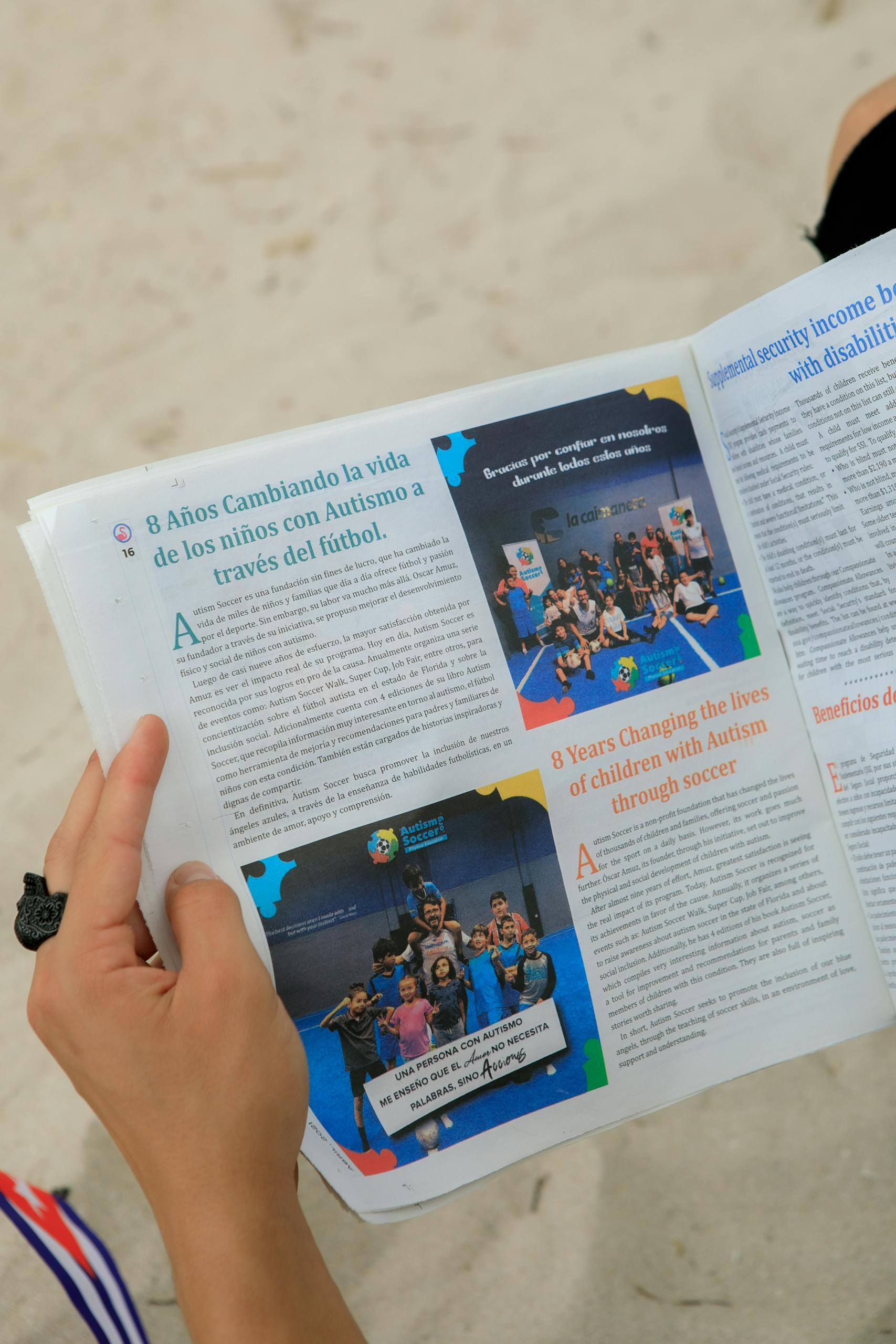 Banaadir News Somalia Close-up of hands holding a magazine about autism support through soccer on a sandy beach.