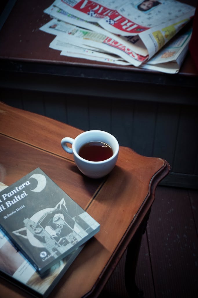 Demolition News Cup of tea on wooden table beside book and newspapers in cozy indoor setting.