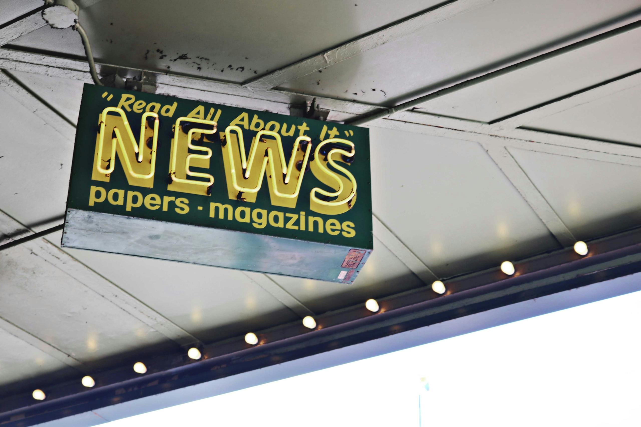 USA Best News Channel PS6 News From below of illuminated signboard with news papers magazines inscriptions hanging on metal ceiling on street