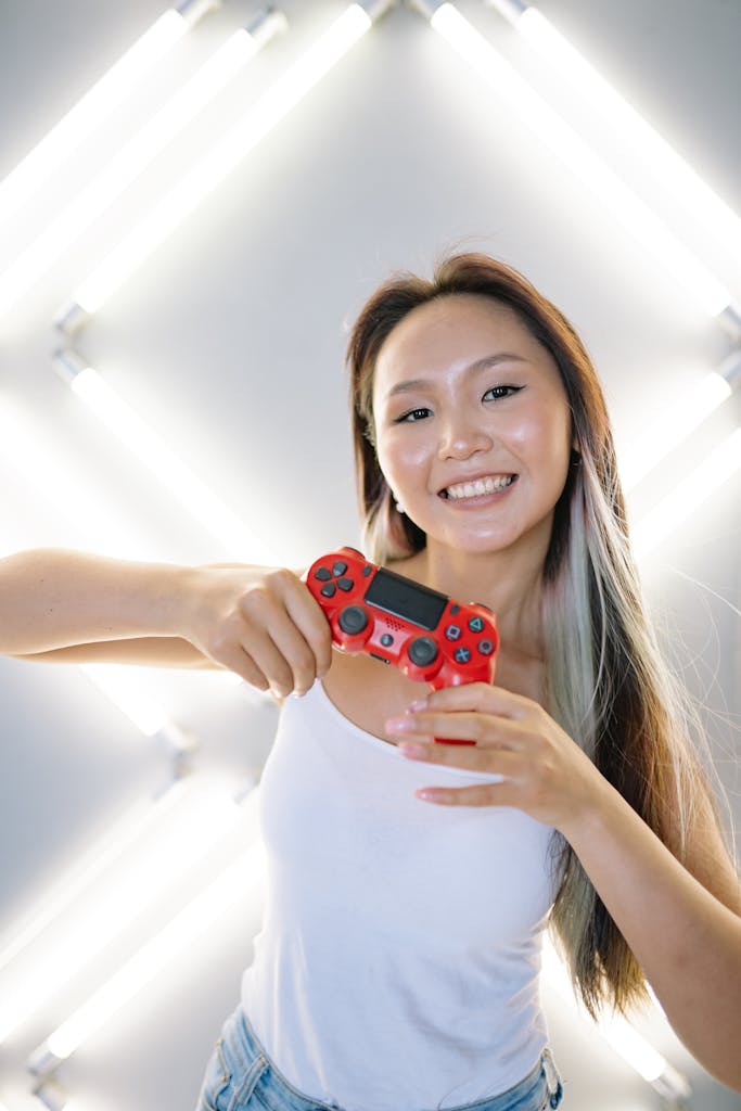 Happy young woman holding a red game controller with a bright smile, standing against a modern light backdrop.