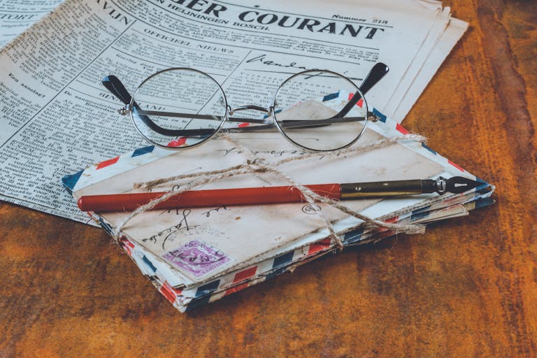 Newspaper The Globe and Mail Historical letters and a fountain pen on a vintage wooden table, alongside eyeglasses and a newspaper.