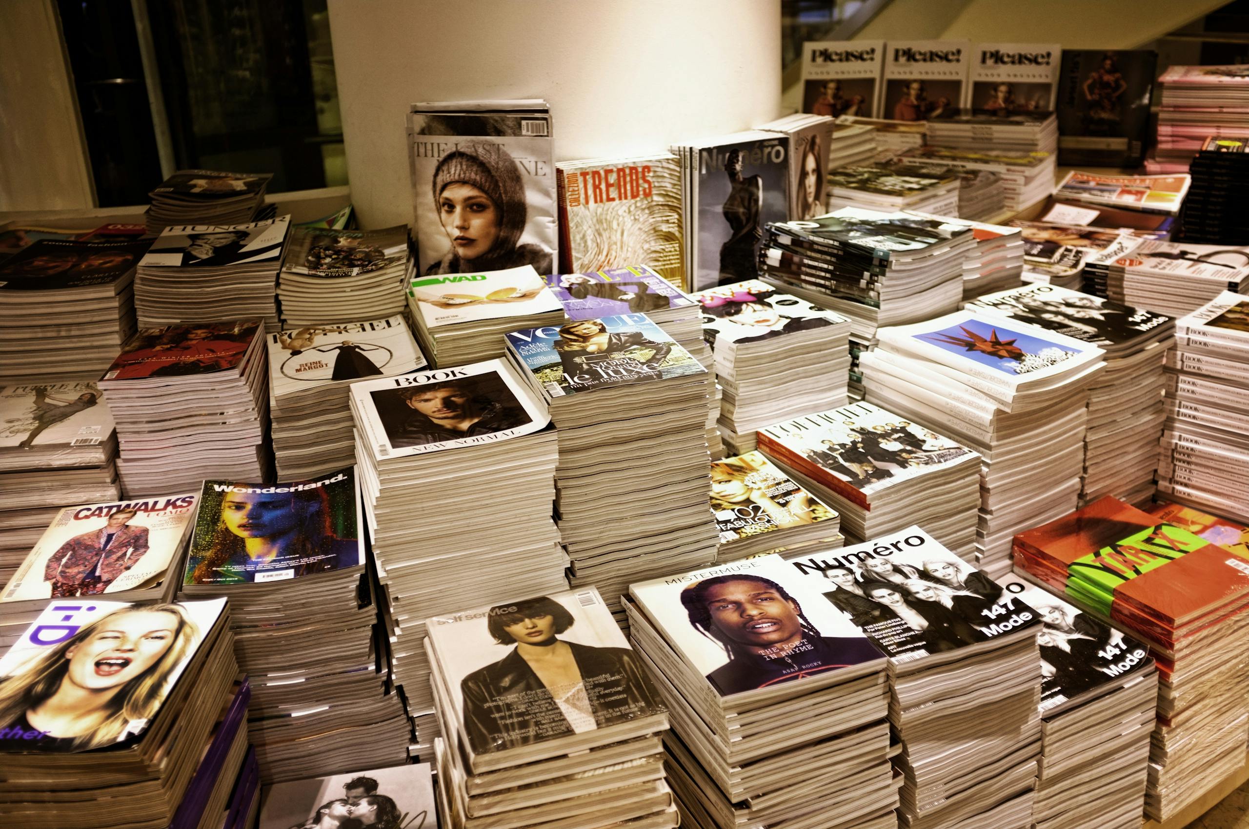 Entertainment News Huge stacks of diverse fashion and lifestyle magazines piled high in an indoor store setting.