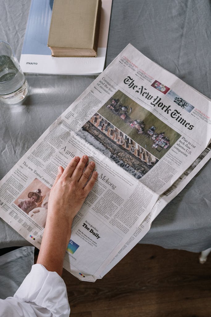 ARY News Person reading The New York Times at home with books and glass of water on the table.