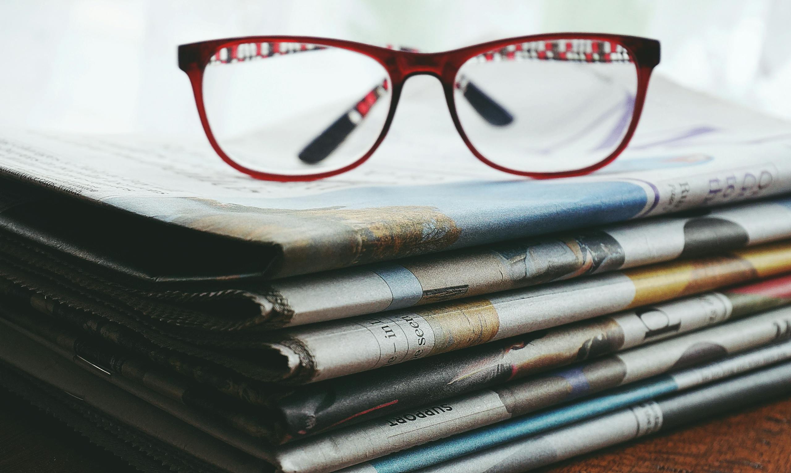 Geo News: Red eyeglasses resting on a stack of newspapers symbolize reading and information.