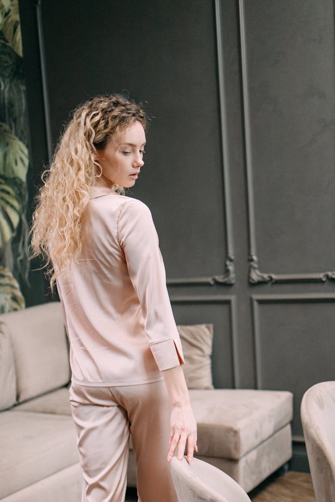 Stylish woman with curly blonde hair in elegant sleepwear, posed stylishly indoors, creating a graceful and sophisticated ambiance.