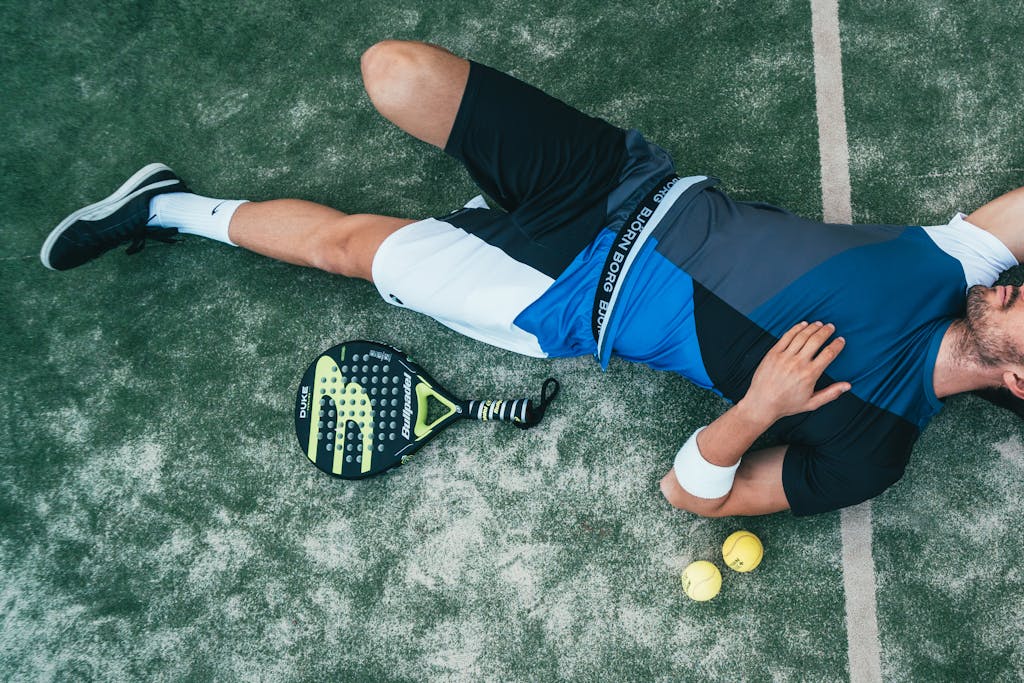 County Sports Tired young athlete resting on padel court with racket and balls nearby.