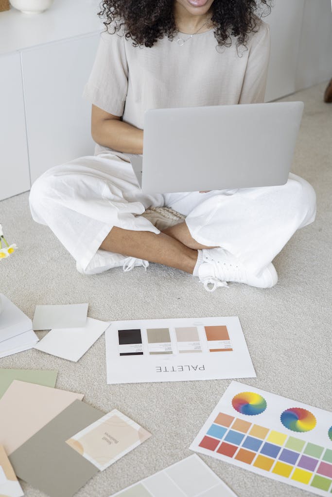 Twastia Com Owner Young woman reviews color palettes for design project on laptop, sitting indoors.