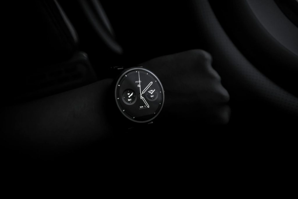 VirtusPlays A sleek Moto 360 smartwatch showing time on a wrist in a dimly lit setting, emphasizing its modern design and technology.