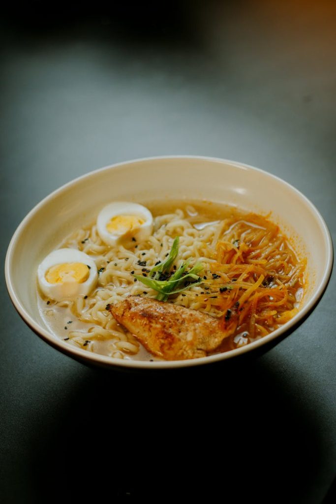 Robert Golob A steaming bowl of ramen with soft-boiled eggs, grilled chicken, and vegetables, perfect for a cozy meal.