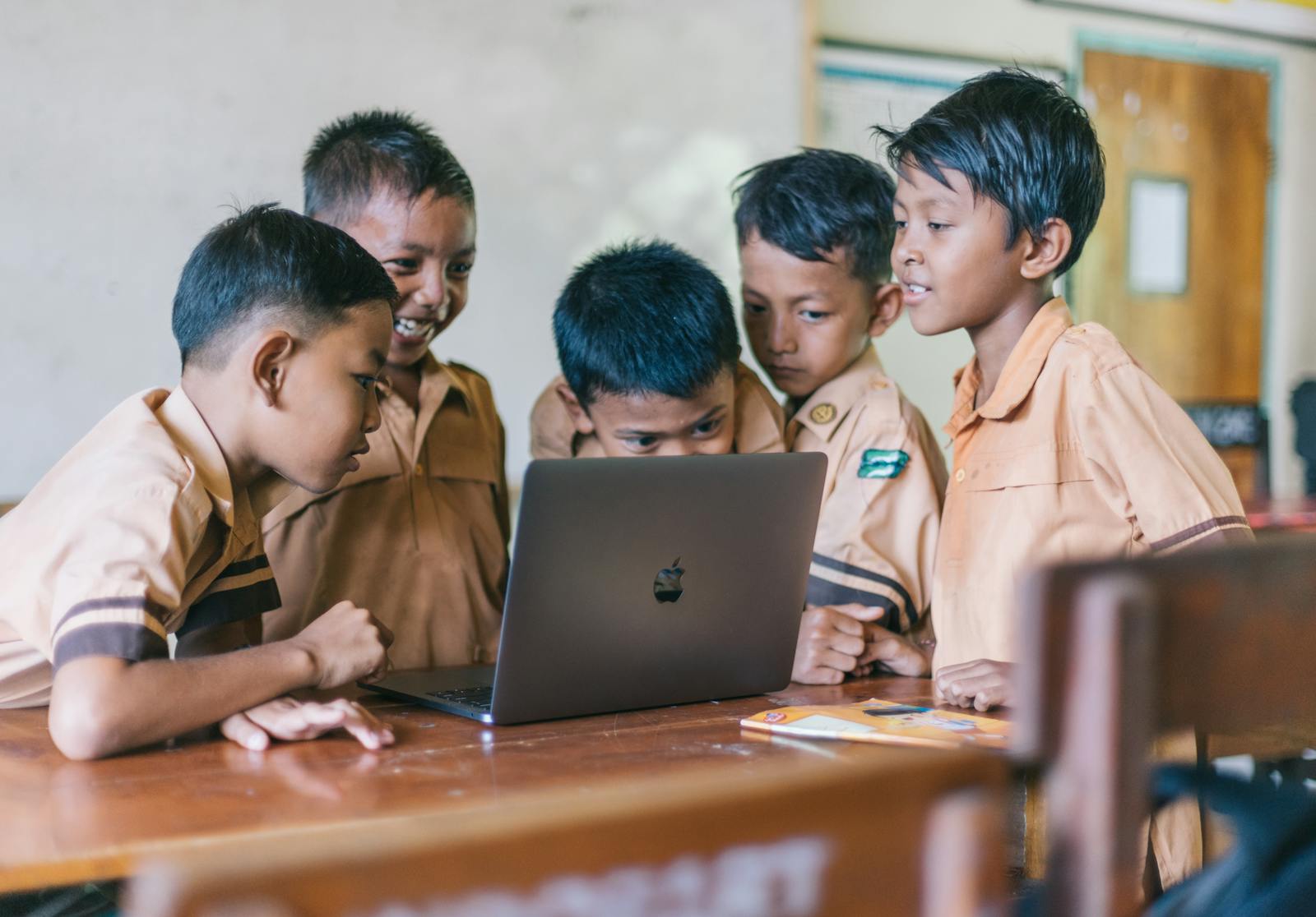 FSI Blogs US A group of young boys in school uniforms collaborating over a laptop in a classroom setting.