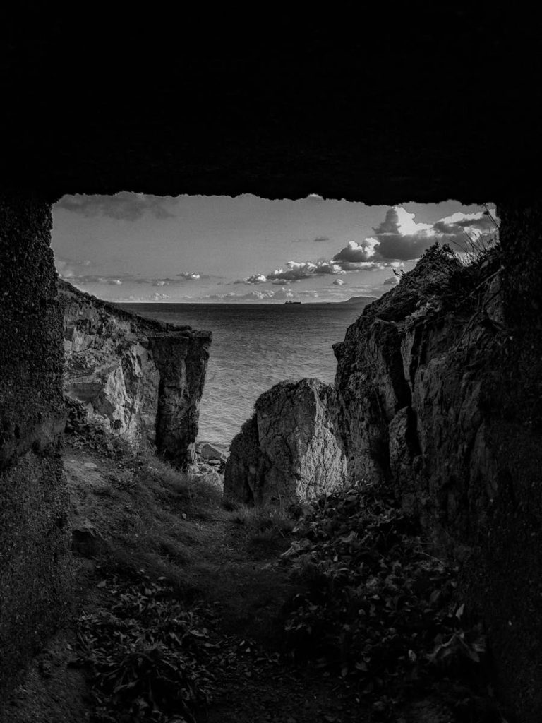 Black and white landscape of a cave overlooking the ocean and cliffs.