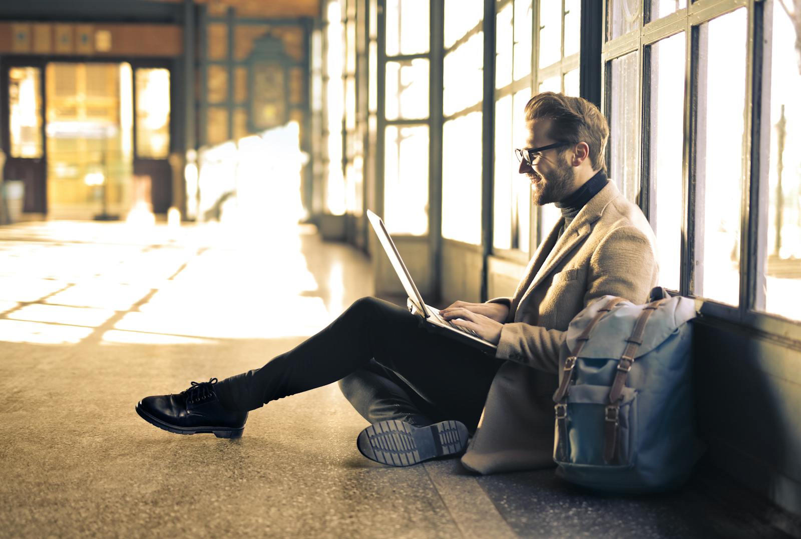 Blazertje Man sitting by a window at a Budapest train station, working on his laptop with sunlight streaming through.
