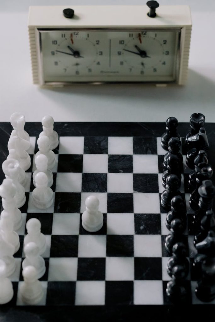 Strategic chess game setup with black and white pieces on a marble board, featuring a classic chess clock.