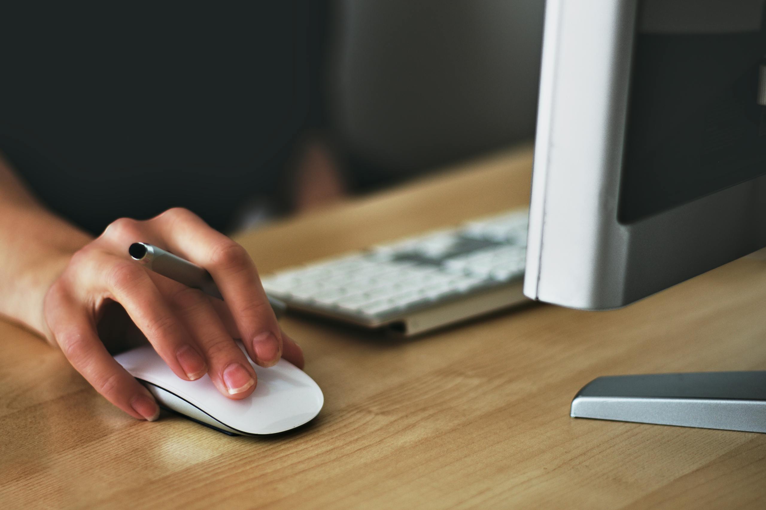 Empowering Employers and Job Seekers A hand using a wireless mouse at a modern desk setup with a computer and keyboard.