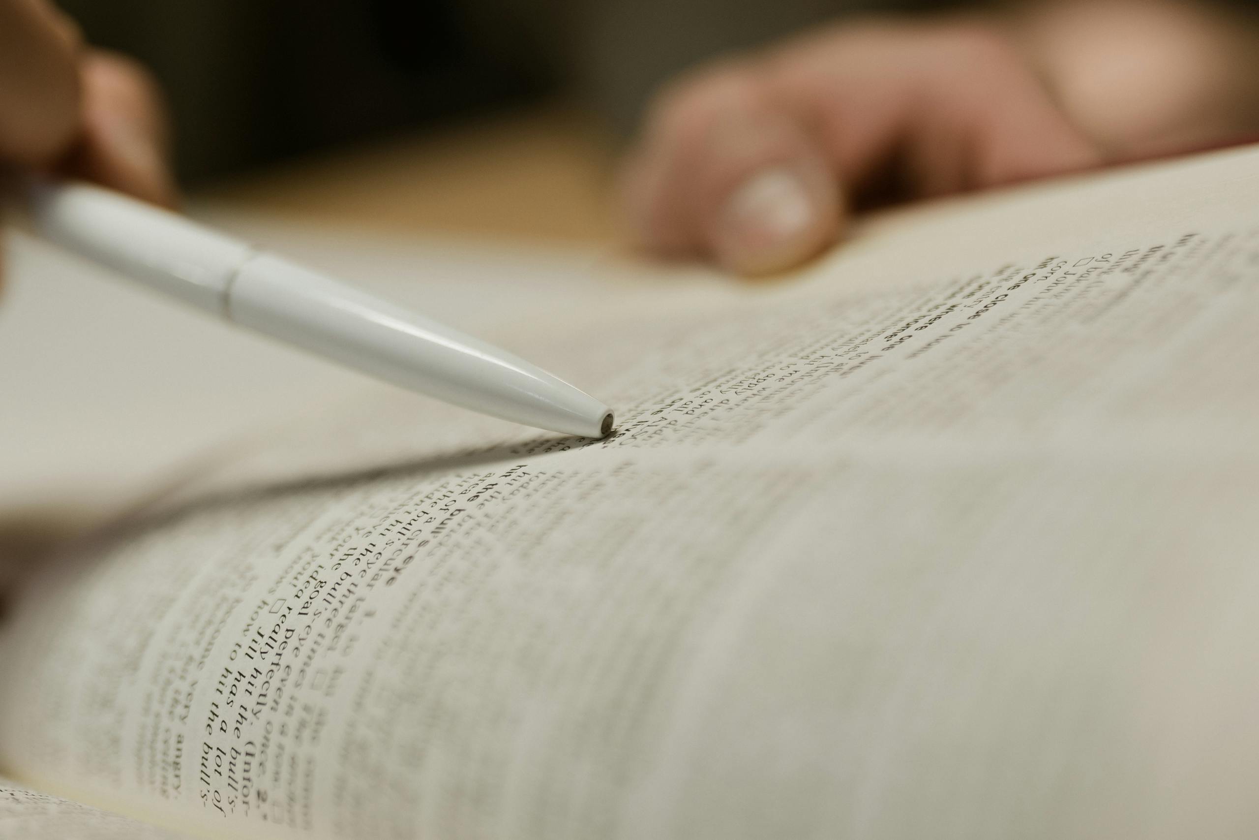 RWU UAR: A person uses a pen to point at text in an open book, focusing on study or research.
