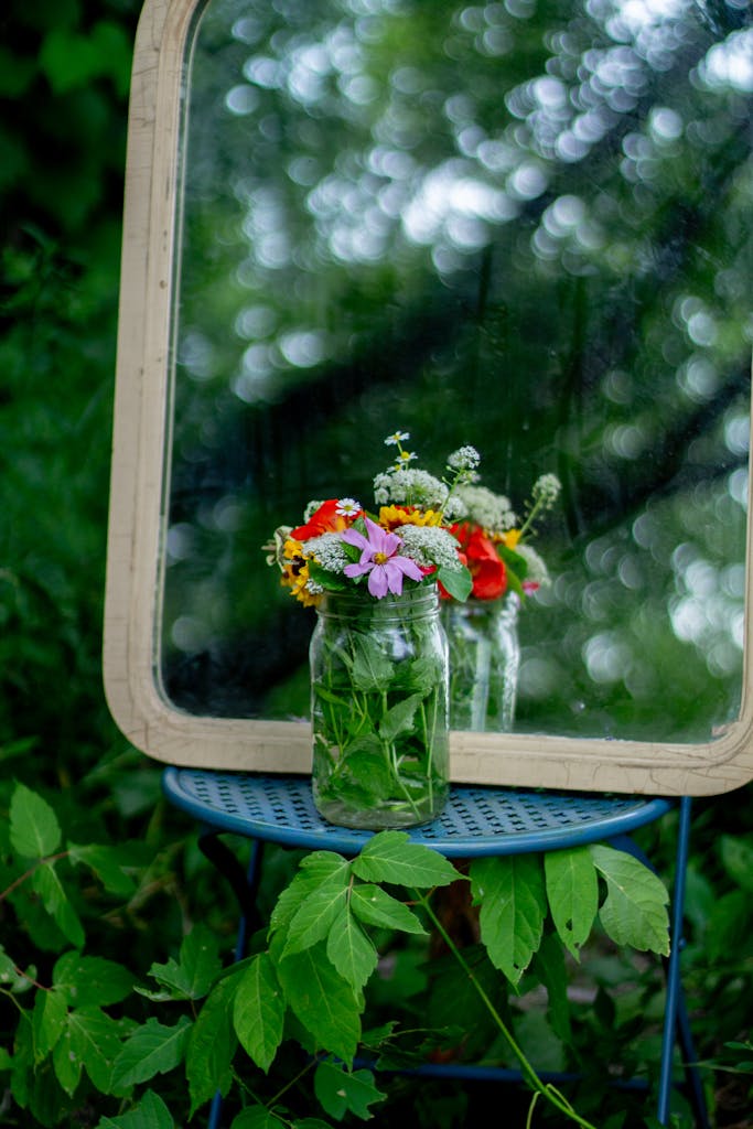 A rustic floral arrangement in a jar, reflected by a mirror, in a forest setting.