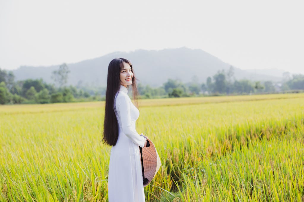 Asian Pinay A woman in a long Vietnamese dress smiles in a vibrant rice field in Hội An, Vietnam.