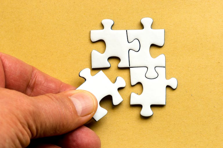 Magento Service Gonzay: Close-up of a hand completing a white jigsaw puzzle on a yellow background.
