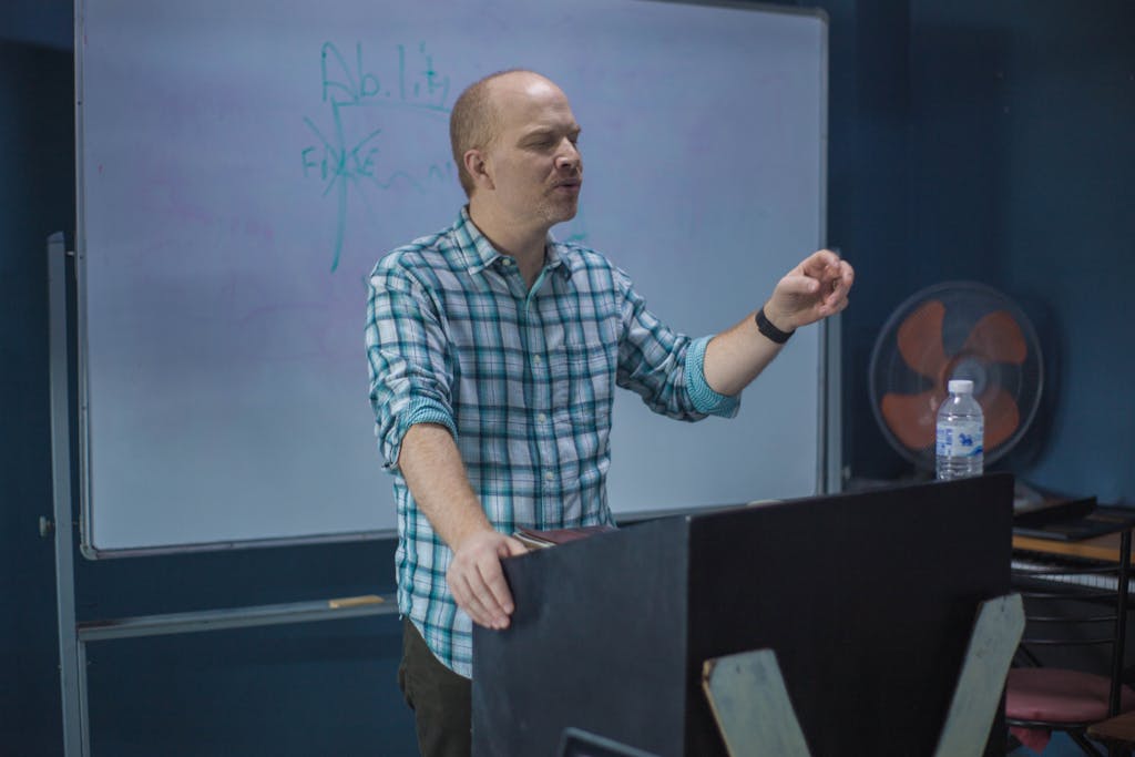 Male lecturer presenting a concept during a university lecture with a whiteboard in the background.