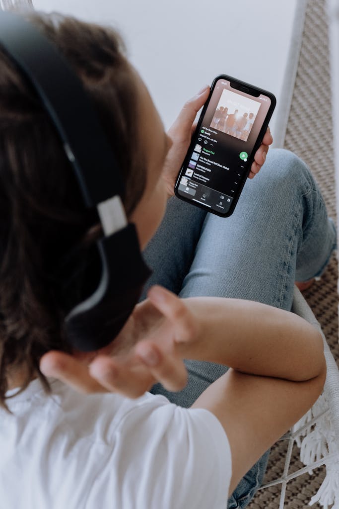 Person wearing headphones, using a smartphone to listen to music in a comfortable setting.