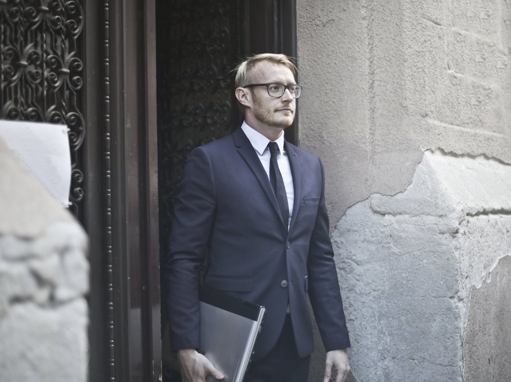 Professional businessman in a suit holding a laptop while standing at a historic doorway.