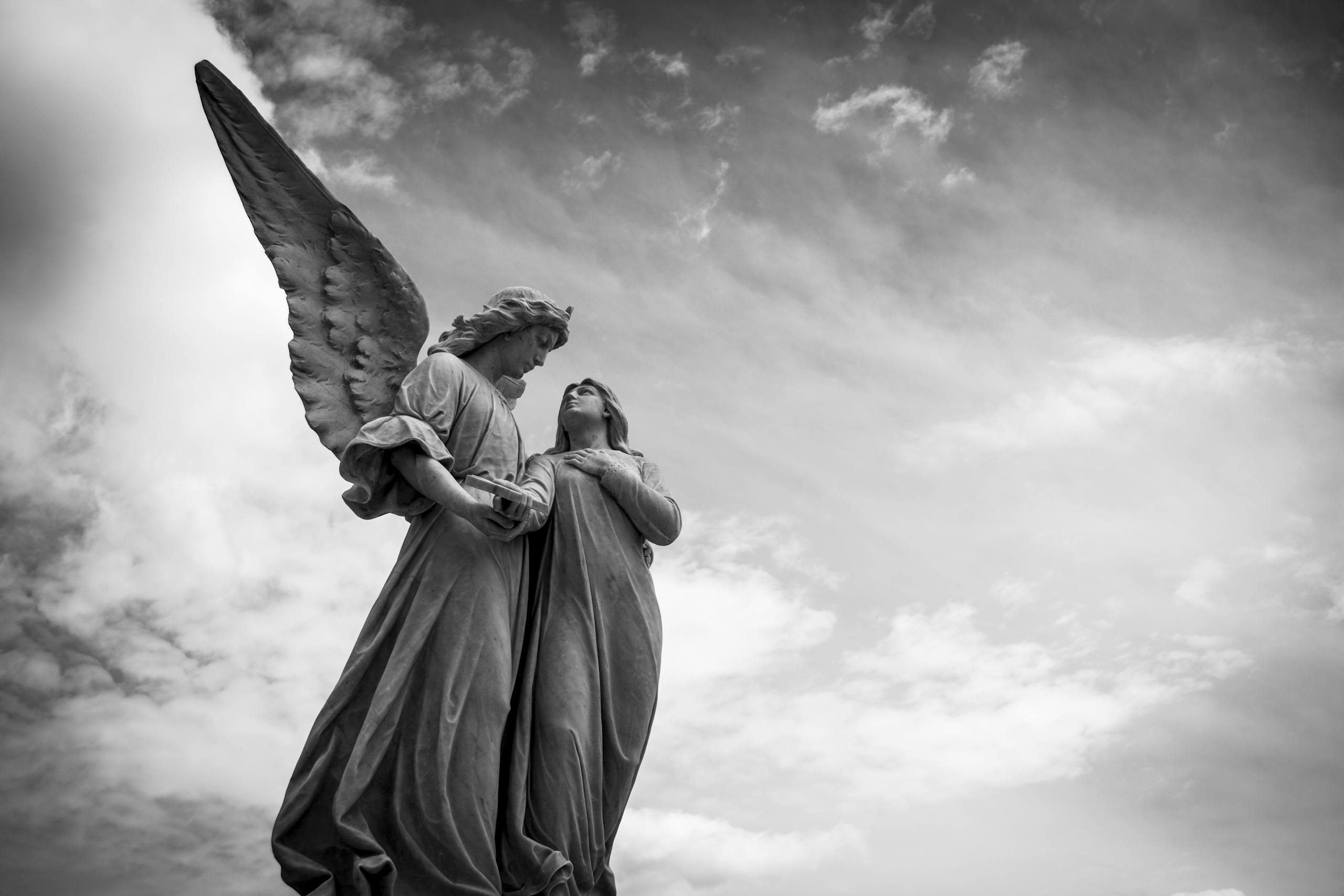 Angel Numbers Striking black and white photo of angelic sculptures under dramatic clouds.