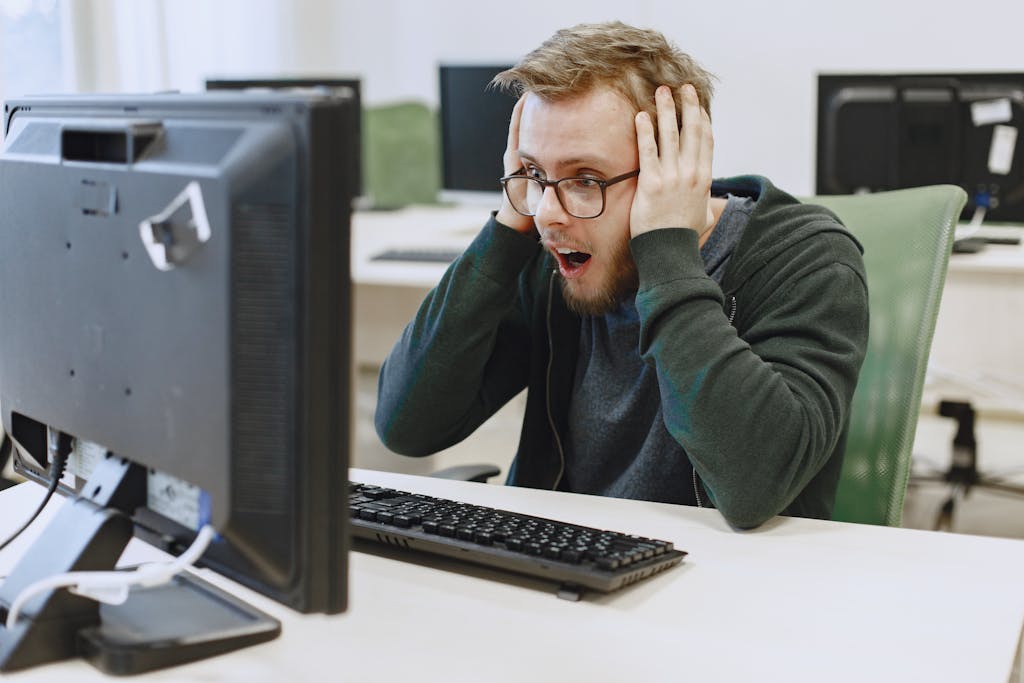 Downnews 
Surprised man in hoodie reacting to shocking news on computer monitor while sitting in a modern office.