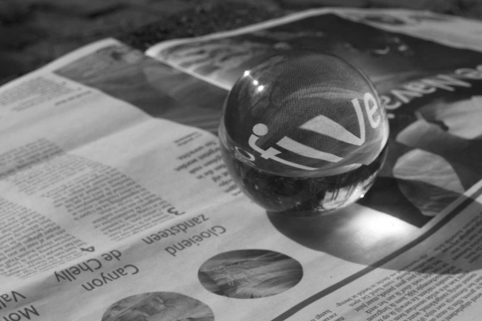 Dolfier A glass sphere magnifies text on a newspaper in a close-up black and white photo.