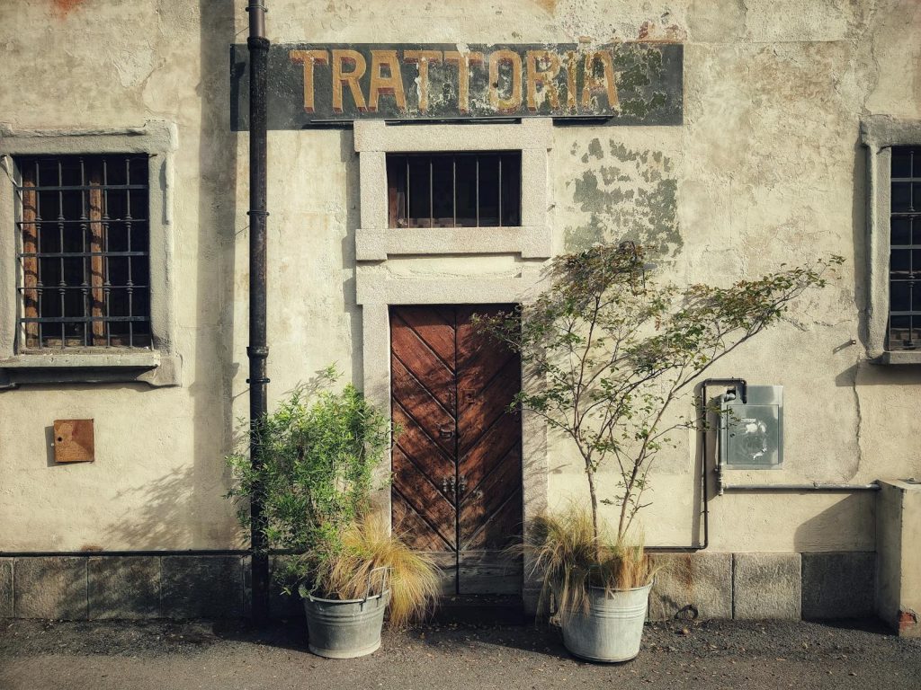 Voozon Vintage Italian trattoria entrance with rustic wooden door and potted plants in Milan's urban scene.