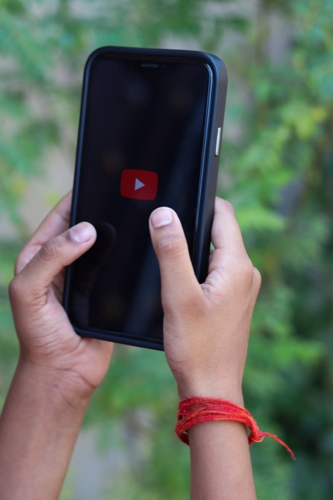 Close-up of hands holding a smartphone showing the YouTube logo outdoors.