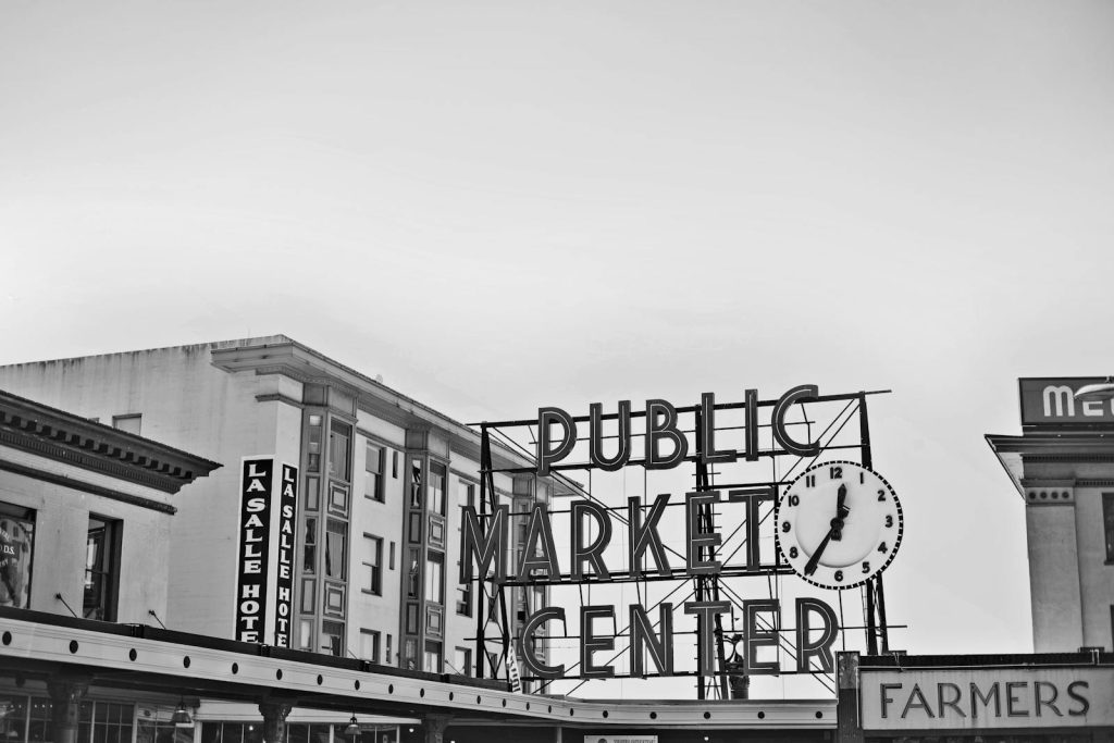 Black and white photo of a public market sign with surrounding architecture.