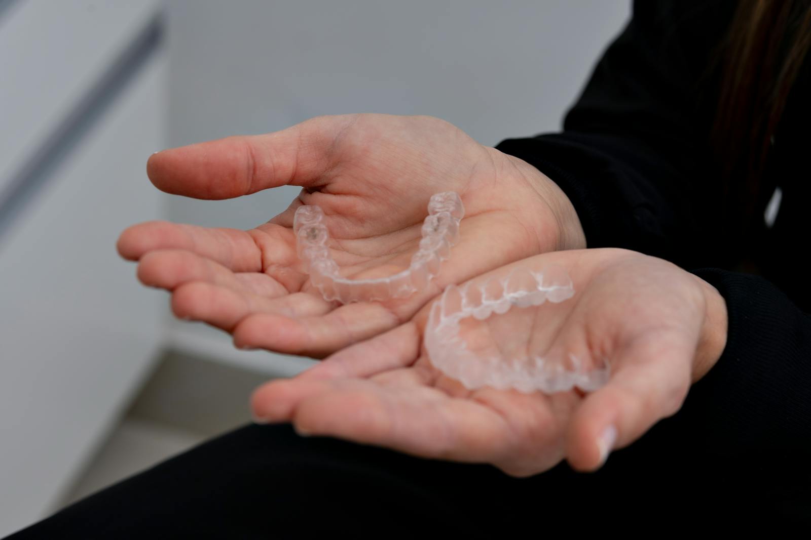 TRIOS 5 Invisalign Submission Close-up of hands holding clear dental aligners in a dental clinic setting.