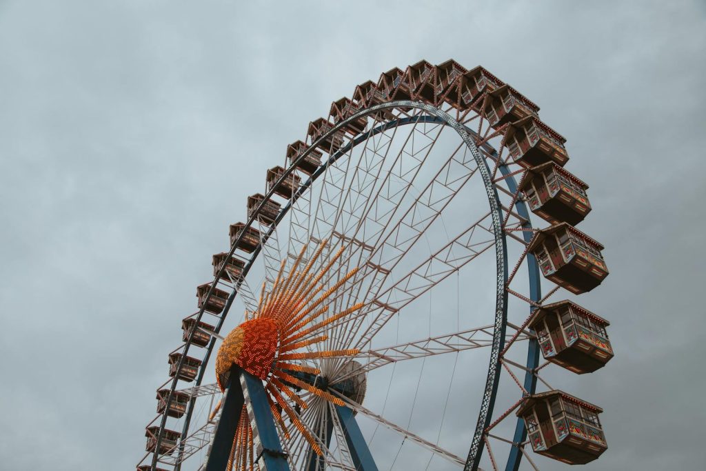 Shop Sunnylife Giant Jumbling Tower  A large Ferris wheel with colorful cabins against a cloudy sky, captured from below.