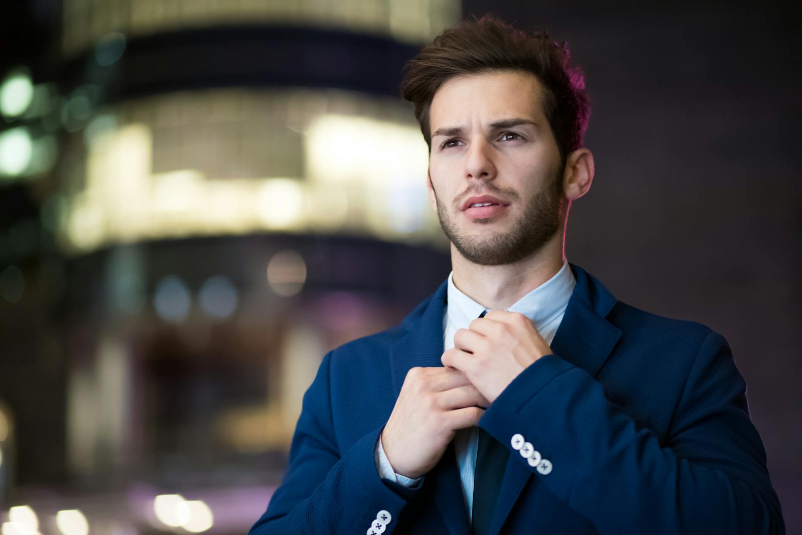 Lidnews Portrait of a stylish businessman adjusting his suit in an urban night setting.