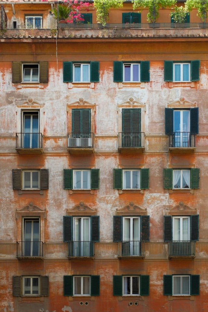 Charming weathered building facade with green shutters and vibrant flowers, capturing classic architecture.