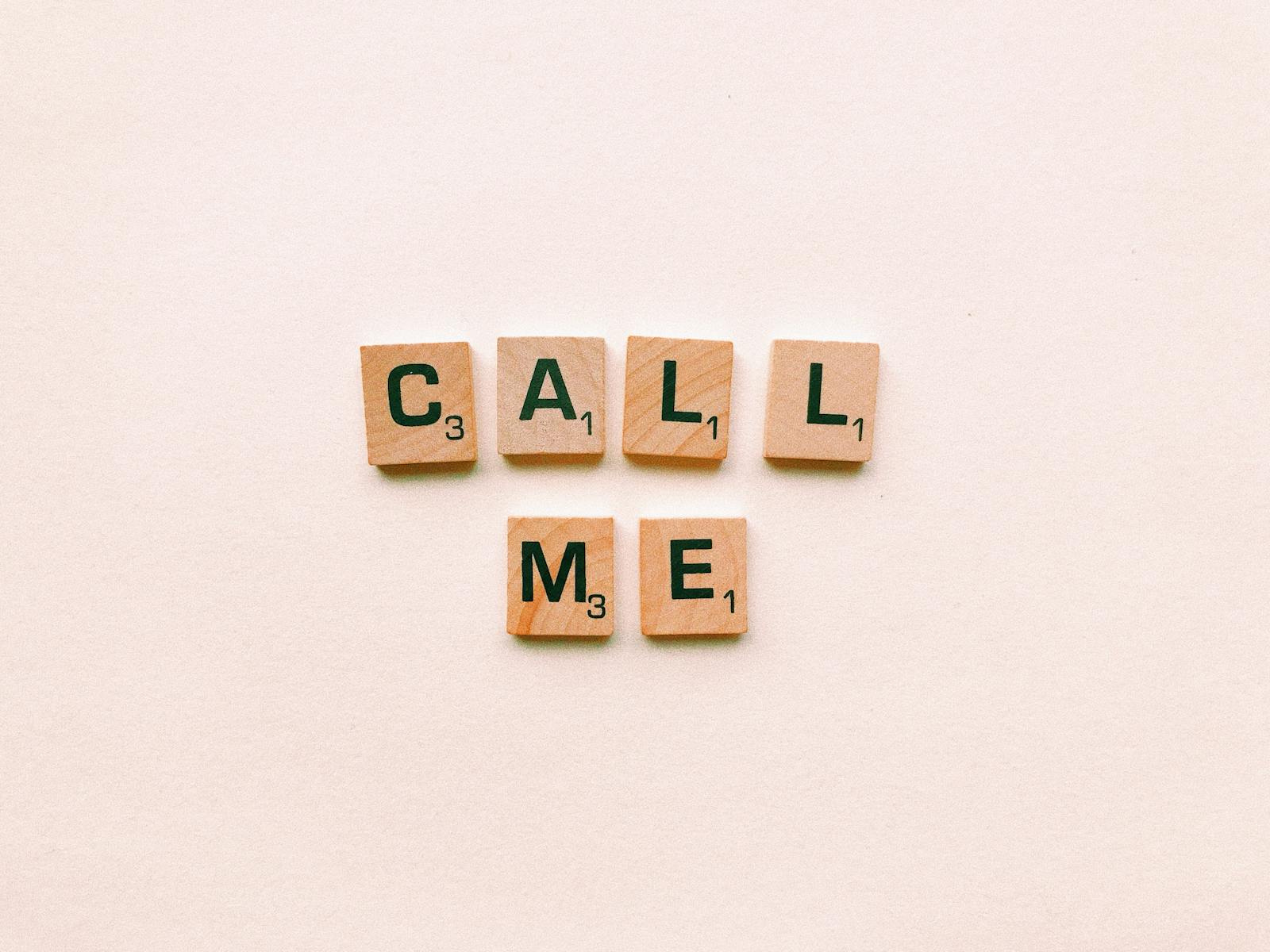 Bolly4u MeWooden letter tiles spelling 'Call Me' on a pastel pink background, invoking communication and connection.