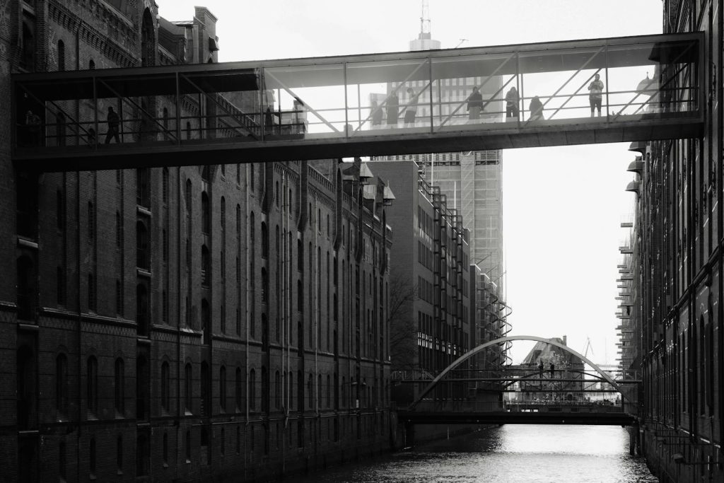 Voozon Black and white view of pedestrians on a bridge in Hamburg's Speicherstadt with canal below.