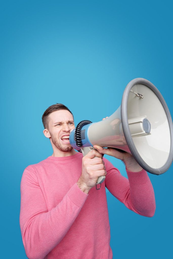 Dynamic image of a man energetically shouting into a megaphone with vibrant blue background and expression of emotion.