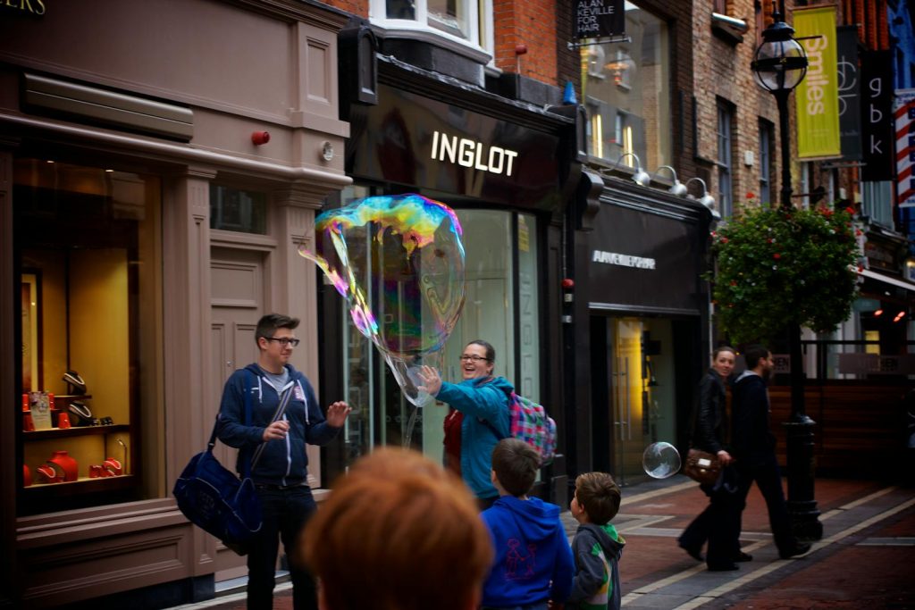 Shop Sunnylife Giant Jumbling Tower Playful scene in a city street with people enjoying a giant soap bubble.